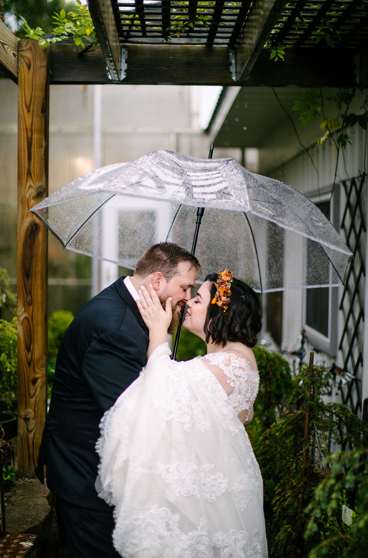 Bride and Groom embrace under clear umbrella at Carol Watson Greenhouse in Lafayette NY