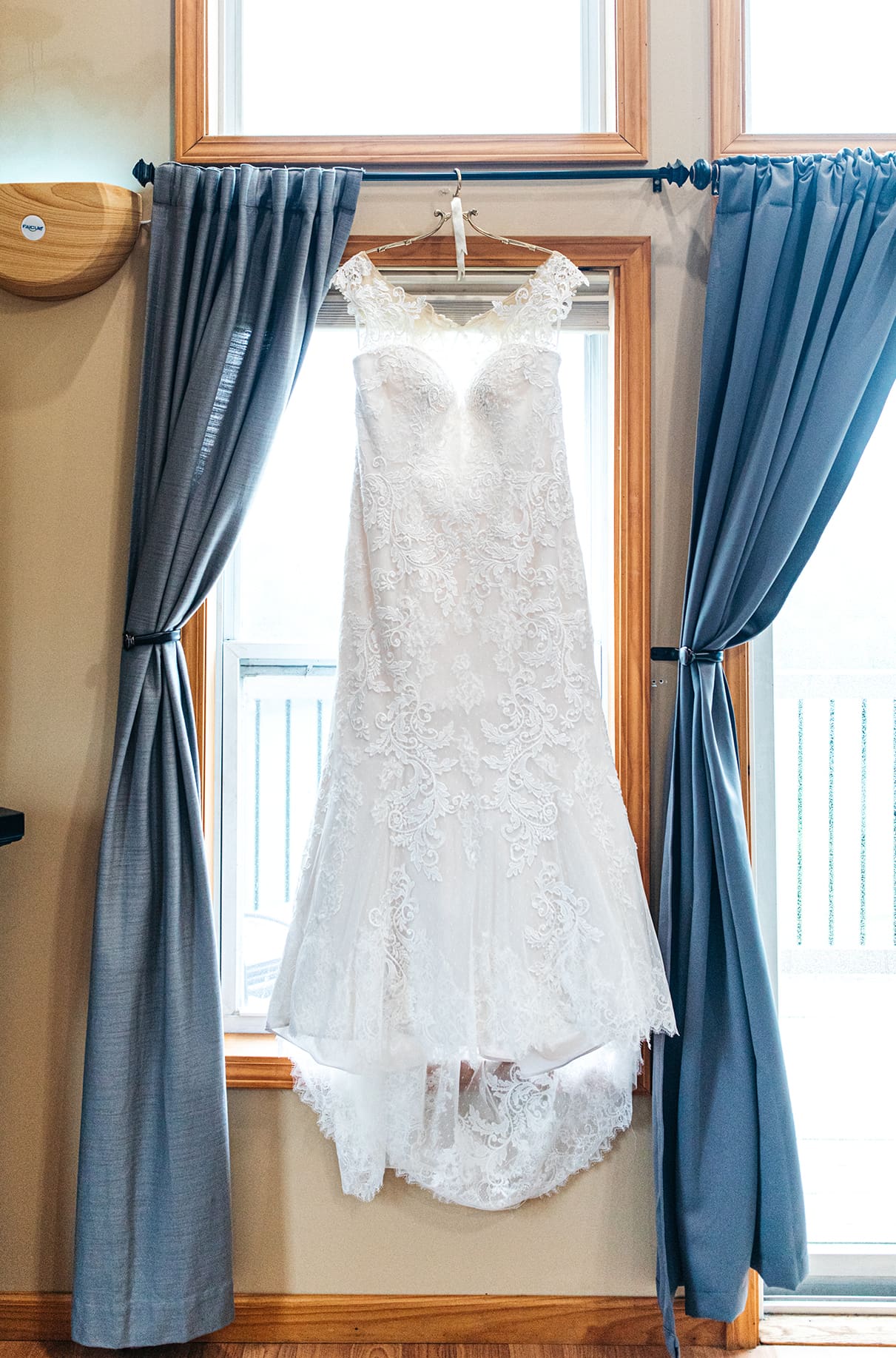wedding dress hanging from gold hanger in window with blue curtains