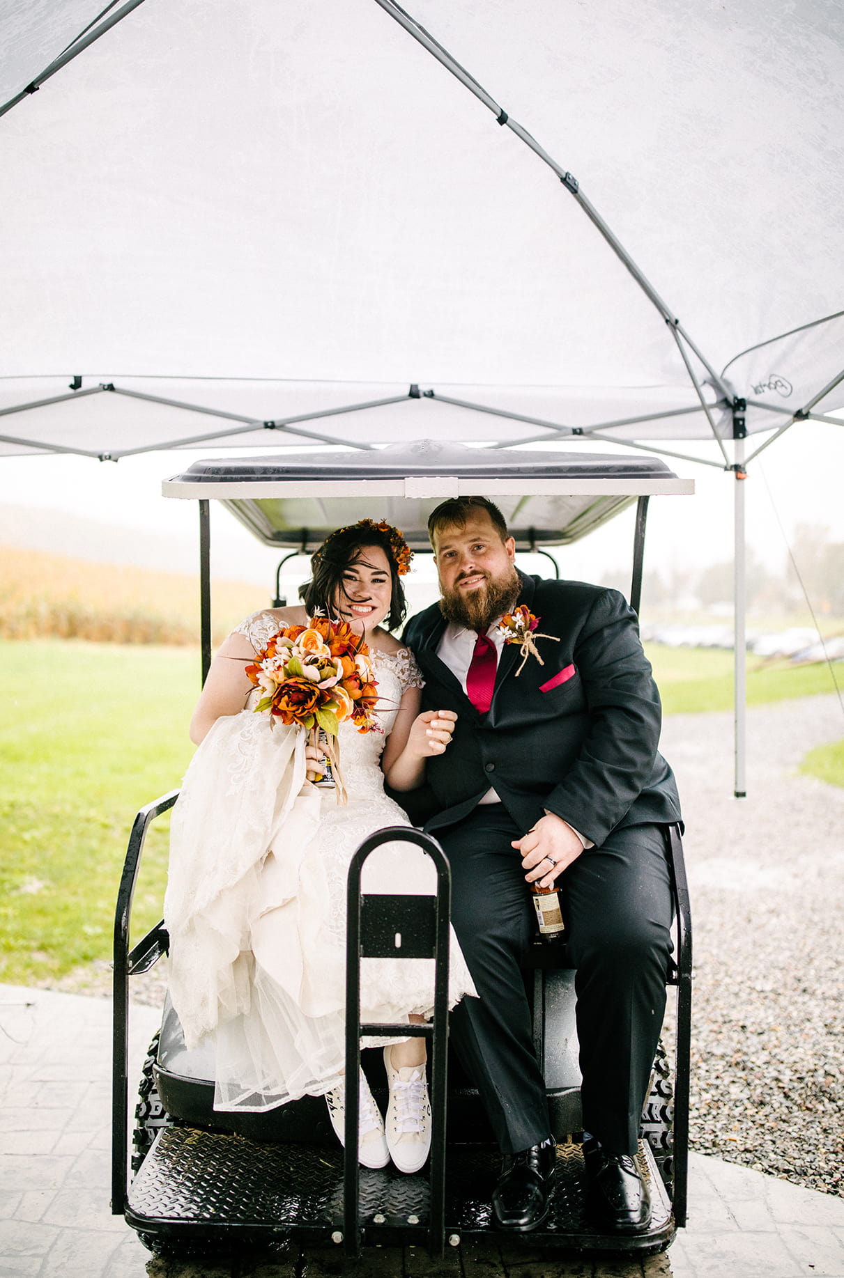 Bride and groom sit in golf cart under a tent on rainy wedding day at Arlington Acres in Lafayette NY