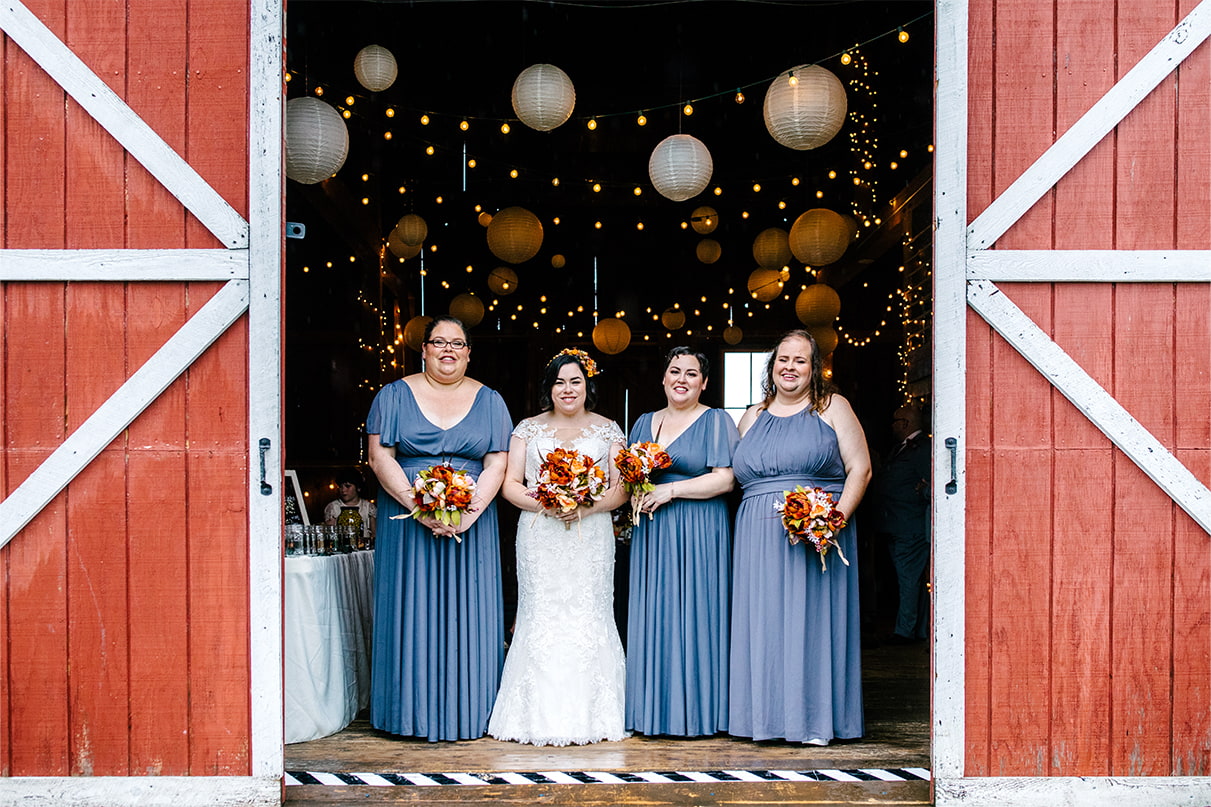 Bride and bridesmaids smile while standing inside barn doors at Arlington Acres in Lafayette NY