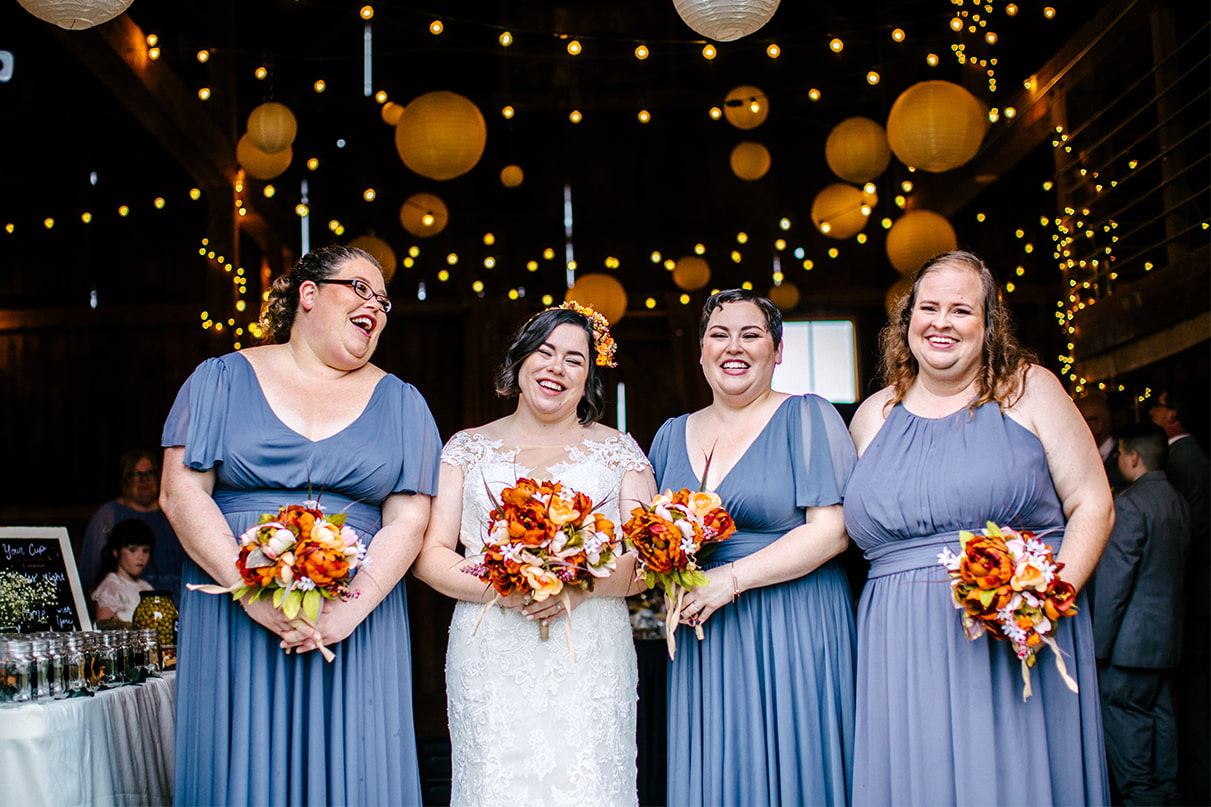 Bride and bridesmaids stand together and laugh inside barn at Arlington Acres in Lafayette NY