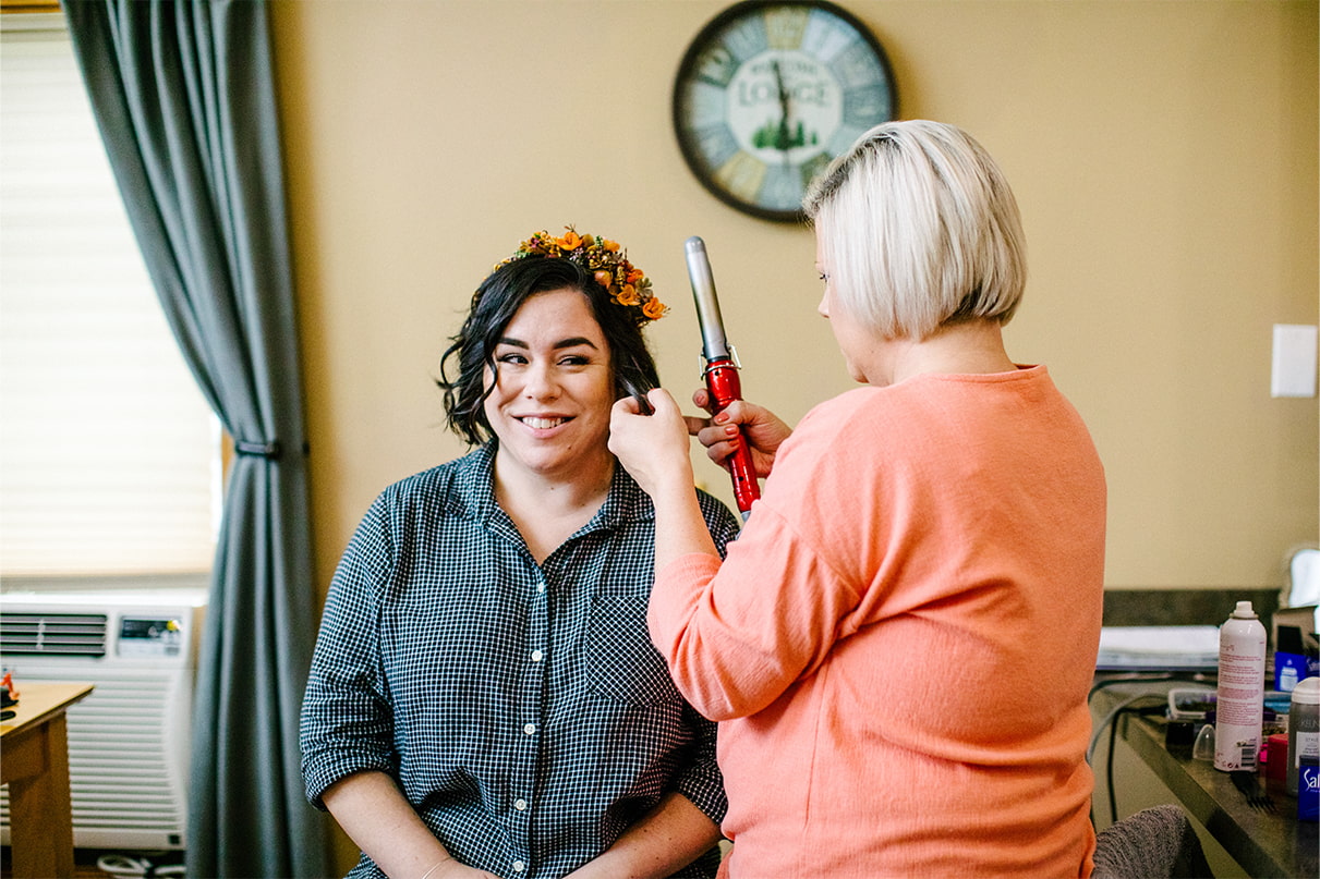 Bride sitting in chair and smiling while hairstylist @hairbykaraerickson does her hair