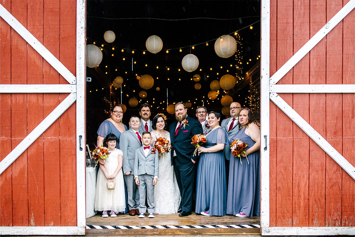 Wedding party stands together and smiles inside of barn at Arlington Acres in Lafayette NY