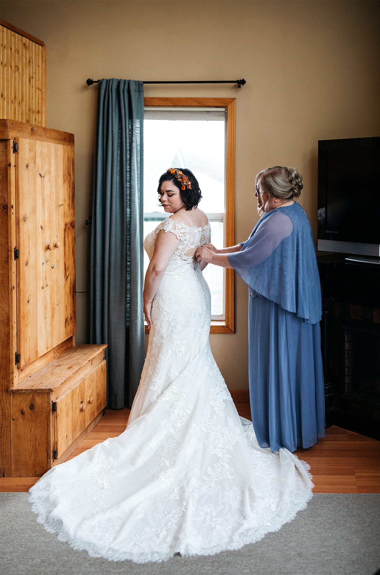Bride stands while mom zips up the back of her dress