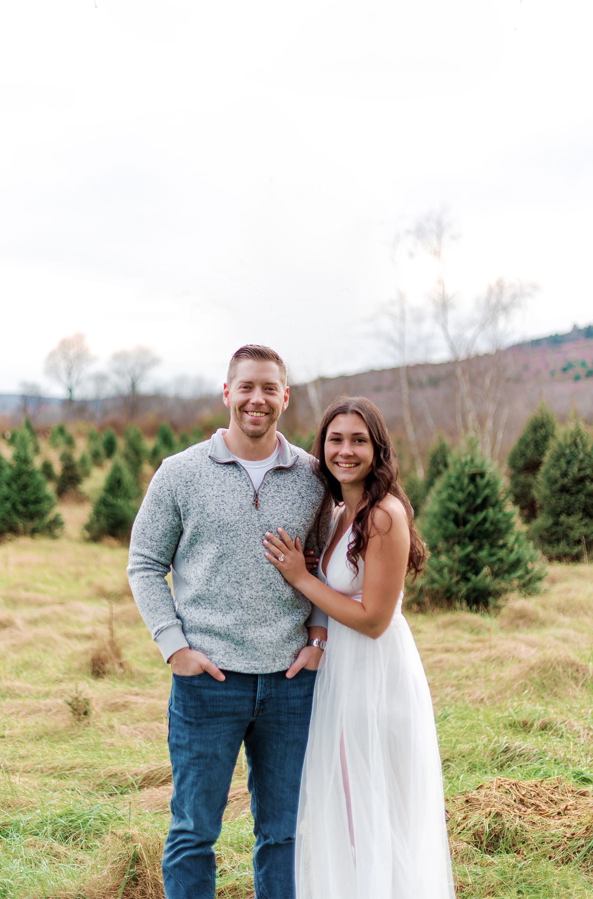 Couple standing together smiling in a field at a Christmas Tree Farm in Bainbridge NY