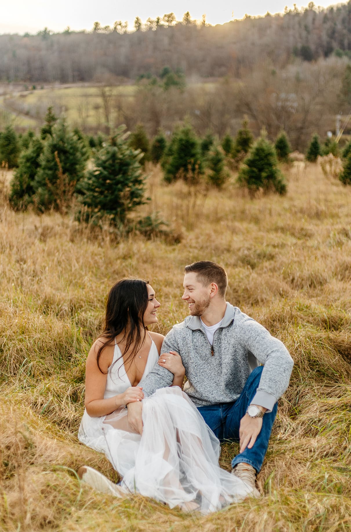Engaged couple sits together in Christmas Tree Farm field at Sipples Farm in Bainbridge NY