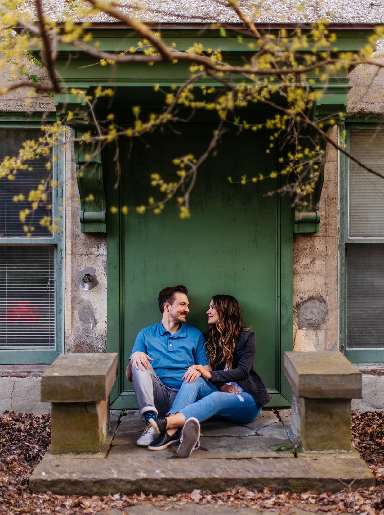 Couple sitting in front of green door during engagement session at Cornell Botanic Gardens in Ithaca NY