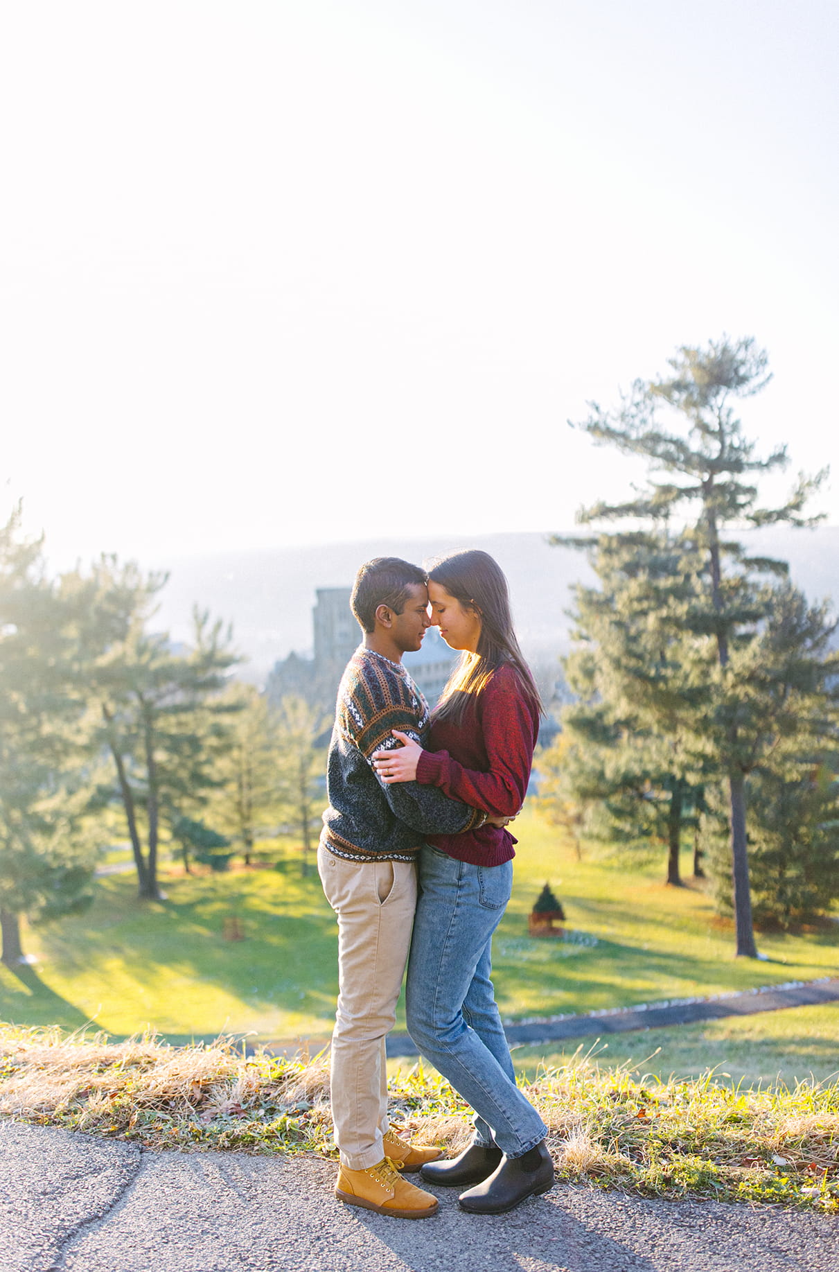Couple embraces during engagement session on hill overlooking the campus of Cornell University in Ithaca, NY