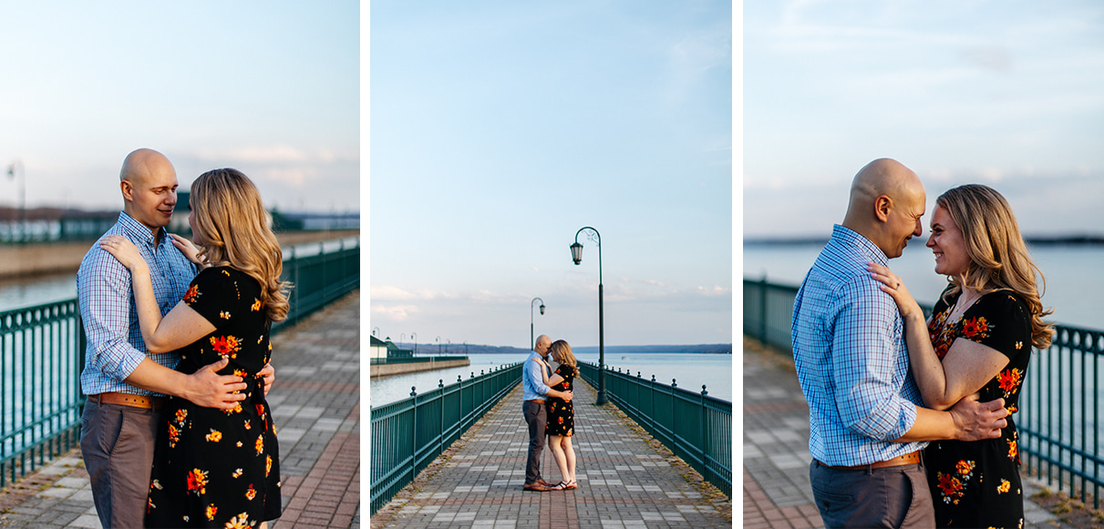 Couple in blue shirt and black floral dress stands on Owasco Lake Pier during engagement session at Emerson Park in Auburn NY