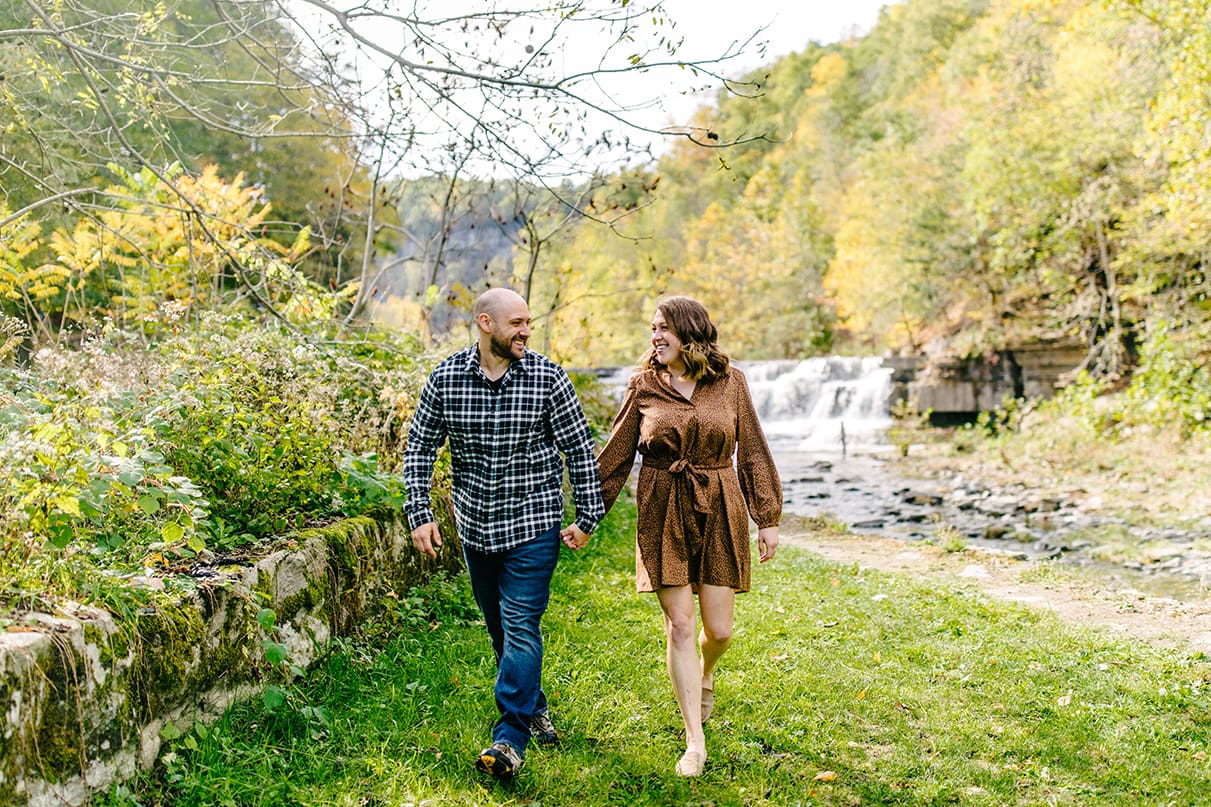 Couple holding hands and walking in front of lower falls at Taughannock Falls State Park in Trumansburg, NY