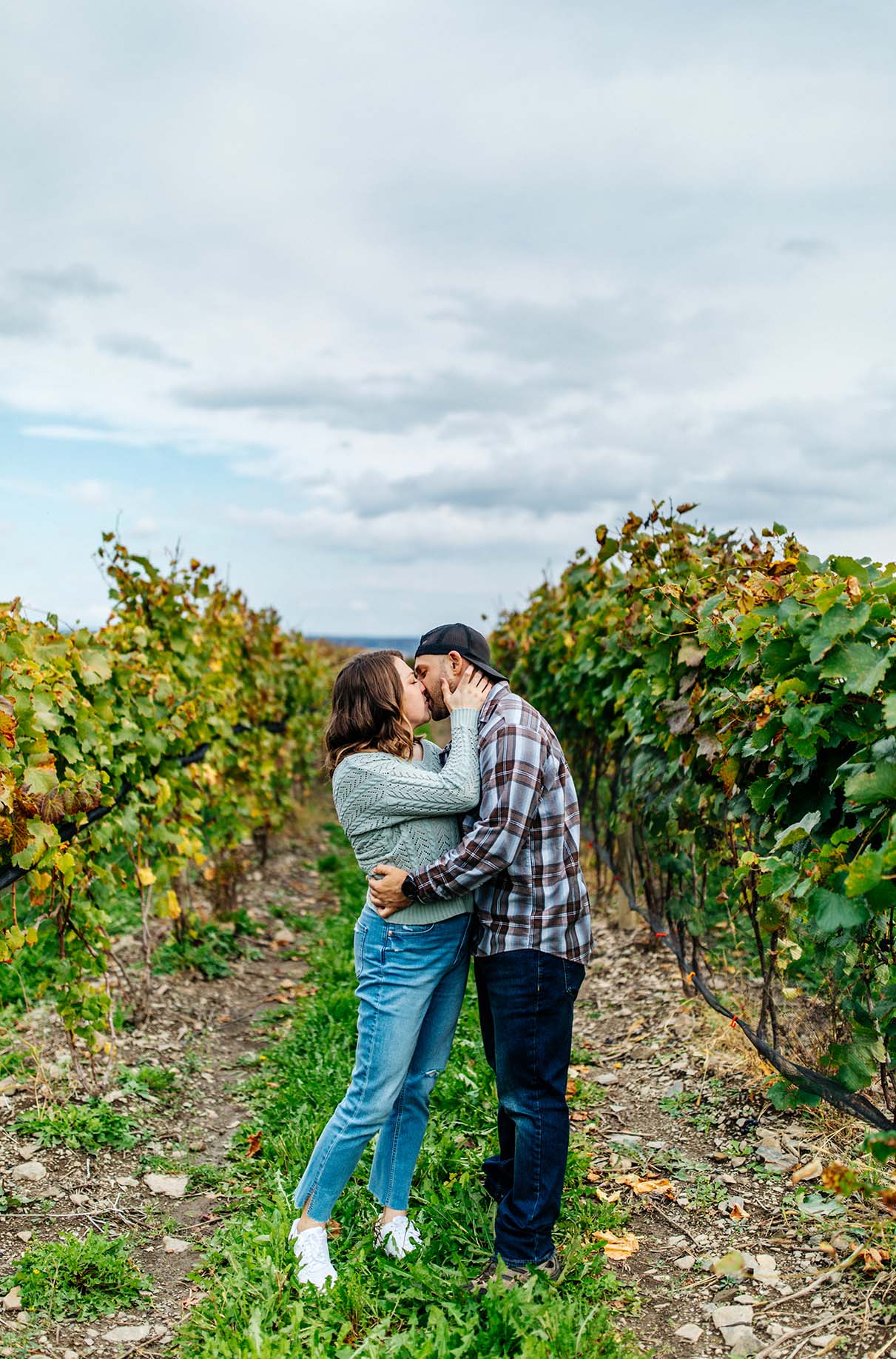 Couple kisses and embraces while standing in vineyard in the Finger Lakes at Bet the Farm Winery in Trumansburg NY