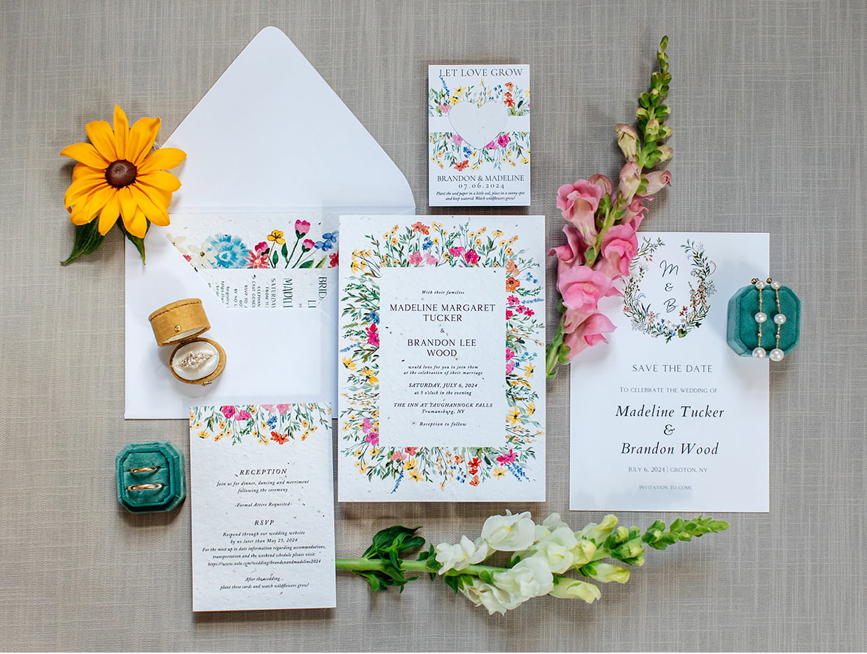 Mostly white invitation suite with small colorful wildflowers on a tan linen background