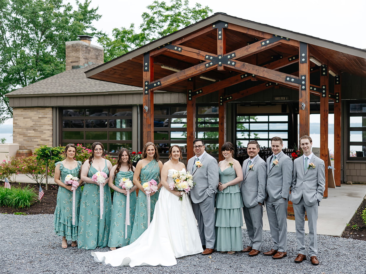 Bride, Groom, and their wedding party smile for a photo standing in front of The Vista at Seneca Lake Resorts in Romulus, NY