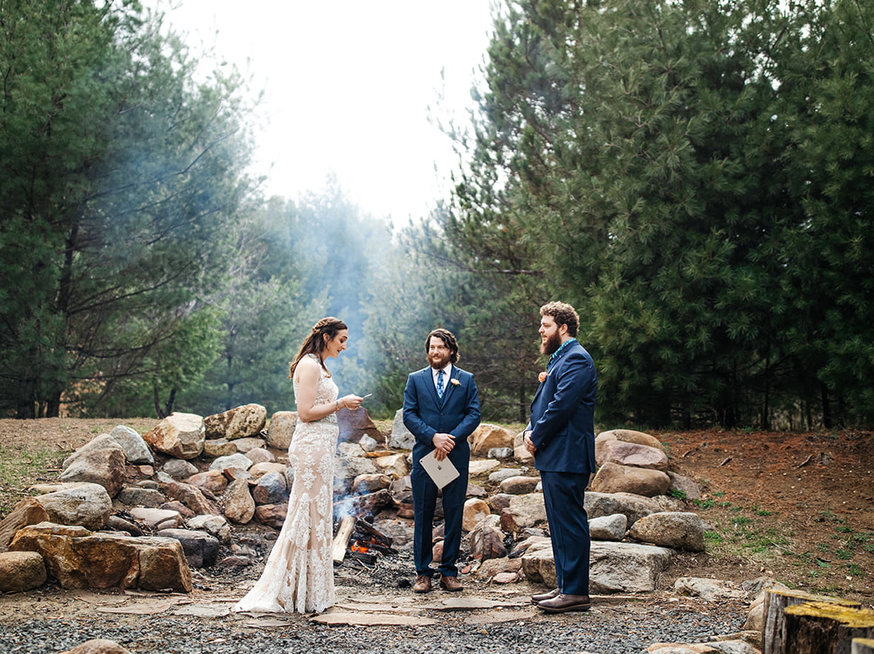 Outdoor wedding ceremony in the Adirondacks set among pine trees and a stone fire pit