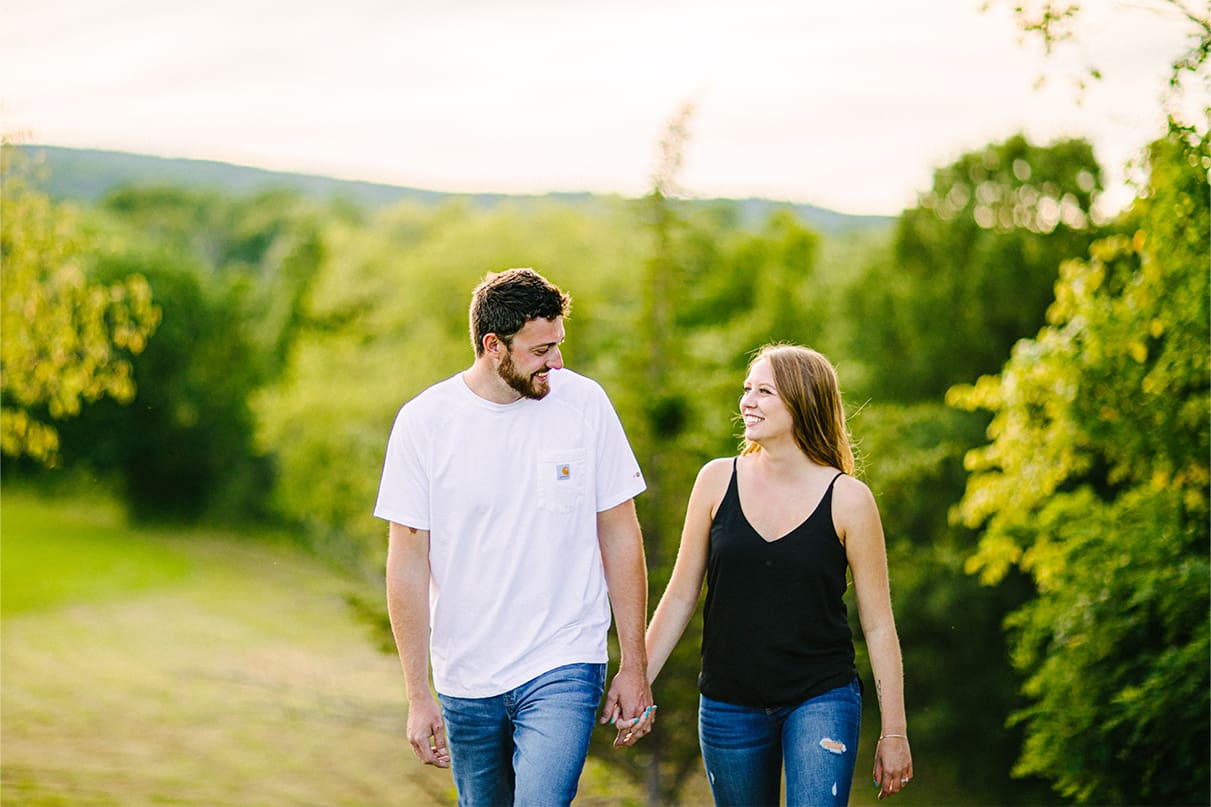 Couple hold hands while smiling and walking up hill during Albany NY Engagement Session