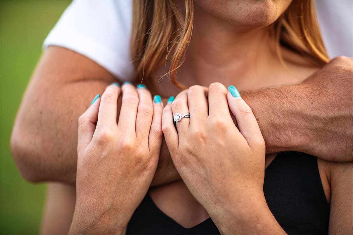 Woman holds onto mans arm while wearing diamond engagement ring