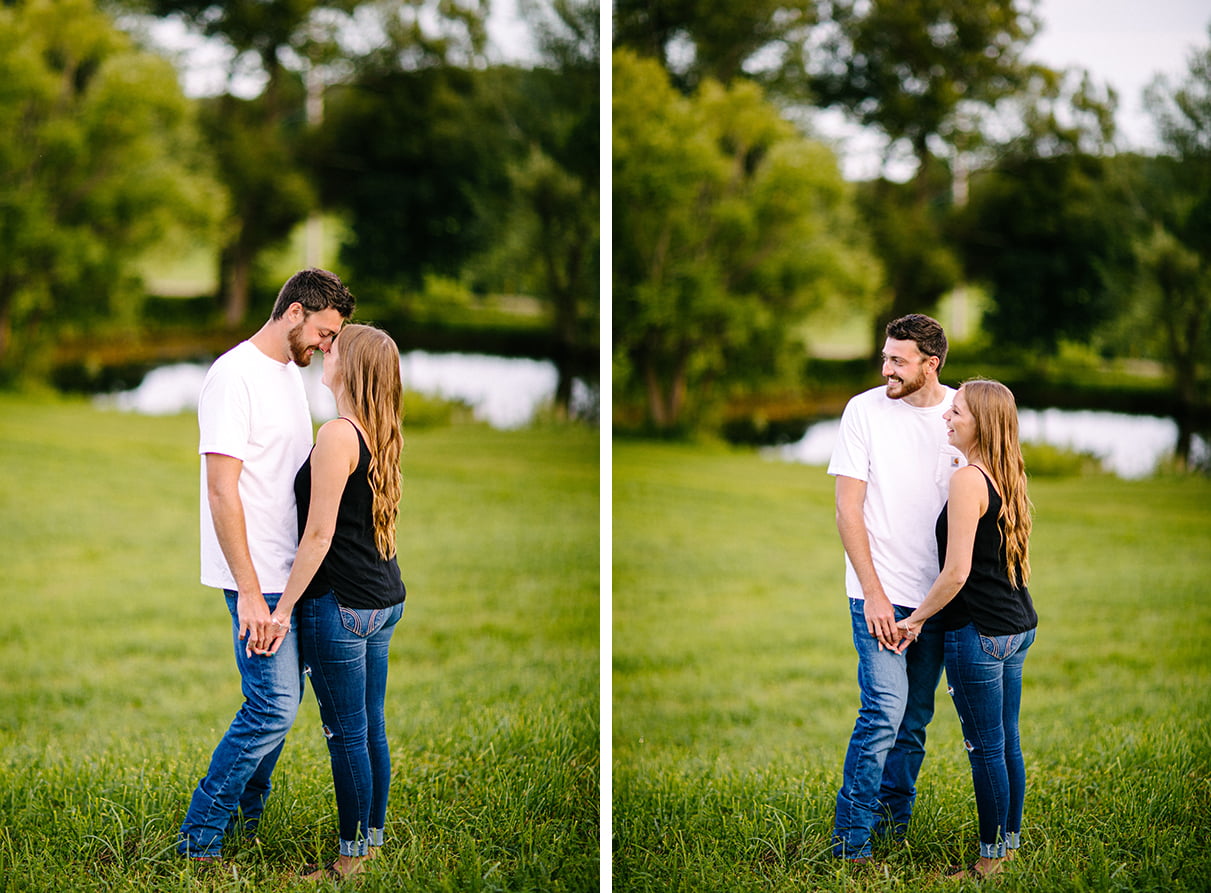 Couple stands on a hill in front of a pond while embracing and smiling