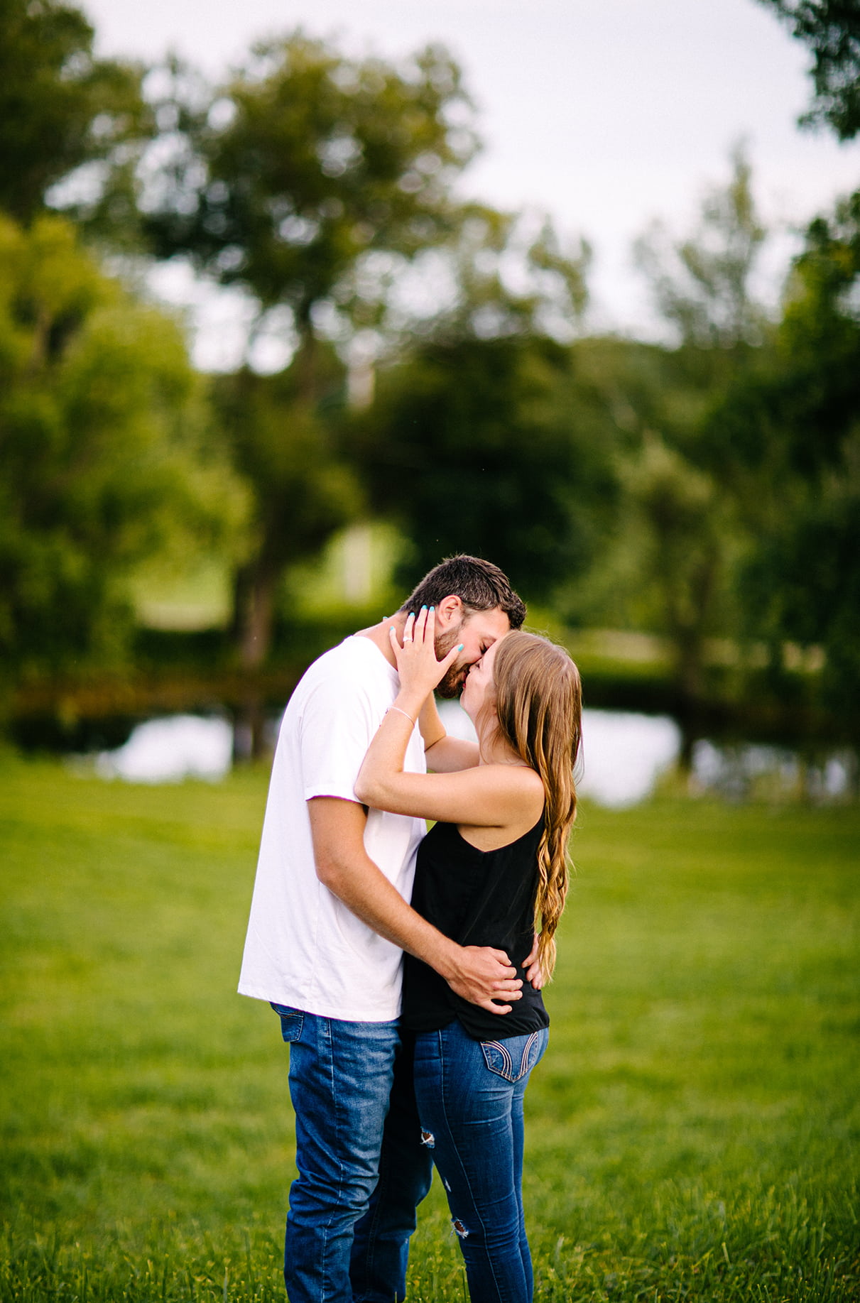 woman pulls mans face down to kiss her while standing on hill in front of pond in Albany NY