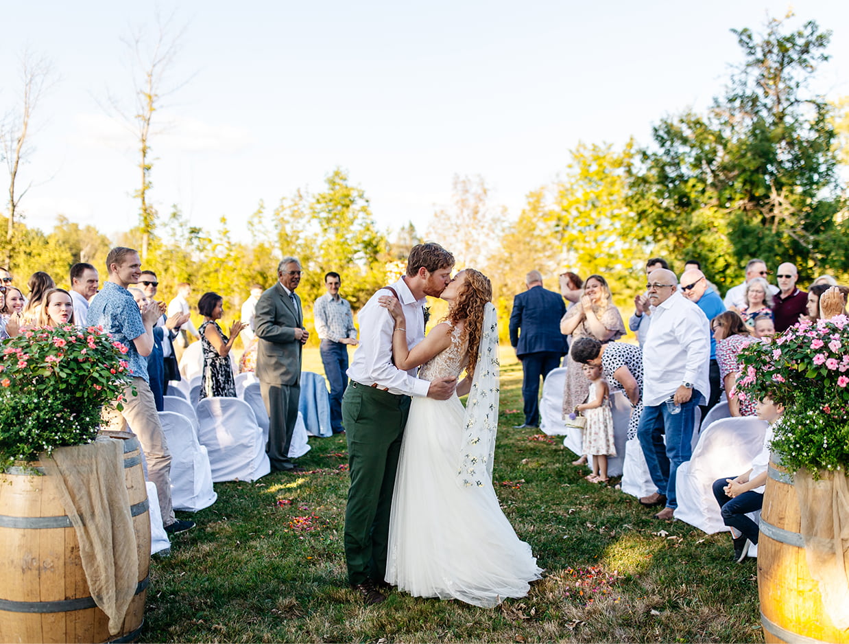 Bride and groom share a kiss at the end of the aisle after their wedding ceremony at Apple Blossom Acres in Freeville NY