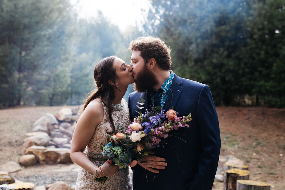 couple kisses in front of bonfire holding colorful bouquet