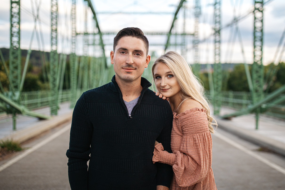 Couple smiles at camera while standing on bridge in Confluence Park Binghamton NY