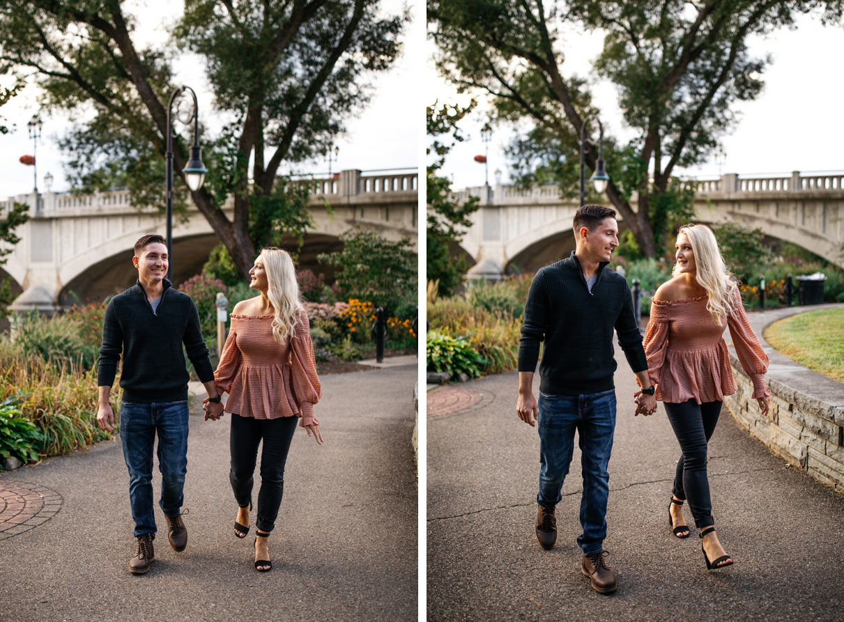 Couple holds hands while walking in front of bridge in  Confluence Park Binghamton NY