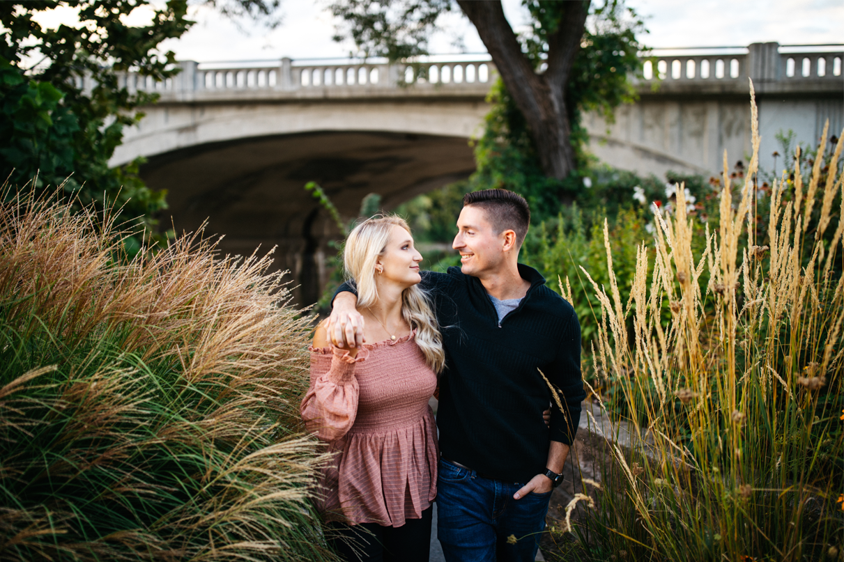 Couple holds hands while walking down lush path