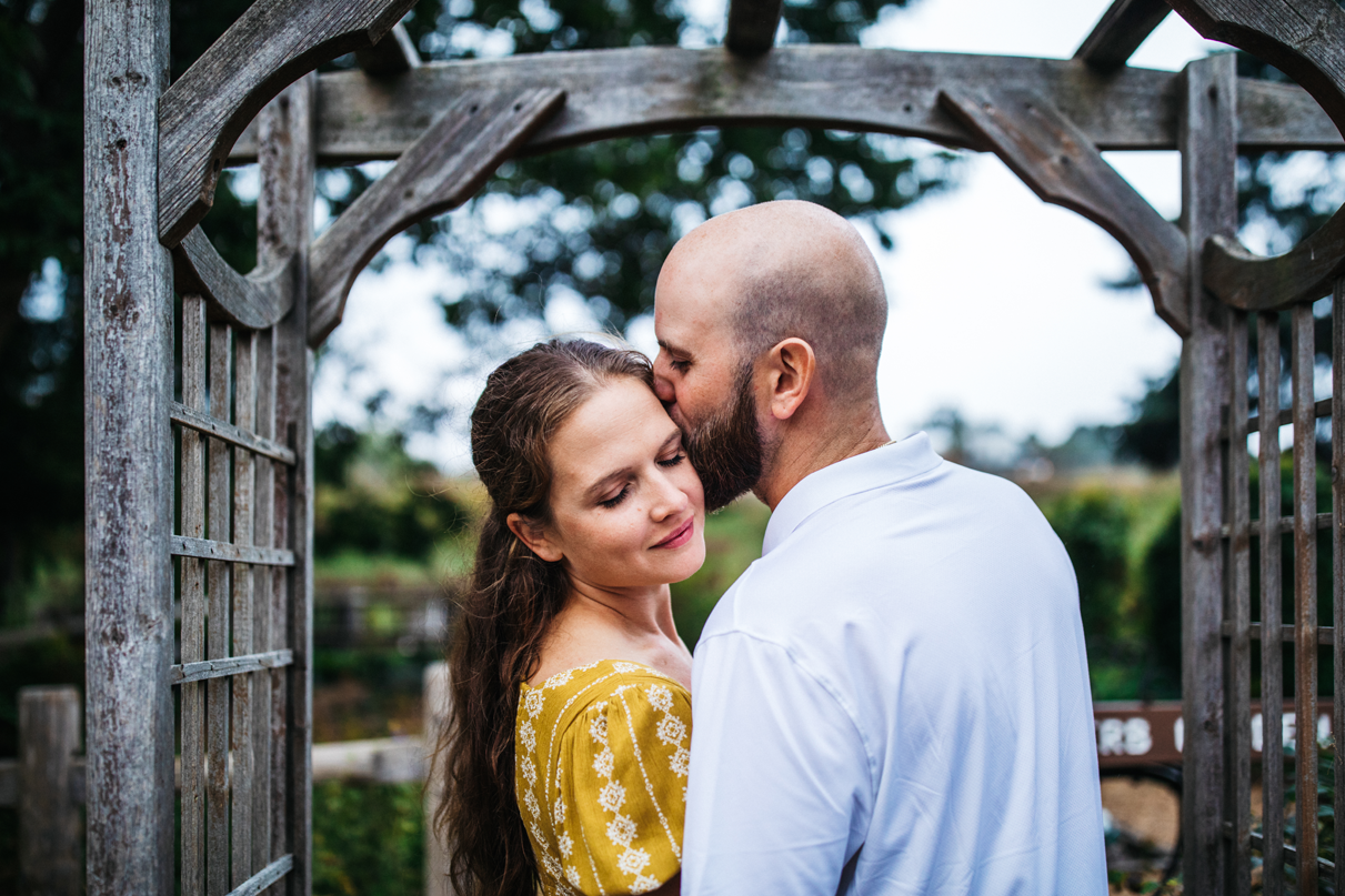 Man kisses womans forehead while standing under a garden trellis