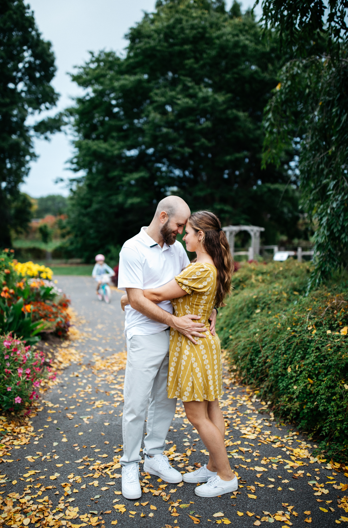 man and woman in yellow dress embrace on path with colorful flowers in botanic garden engagement photo