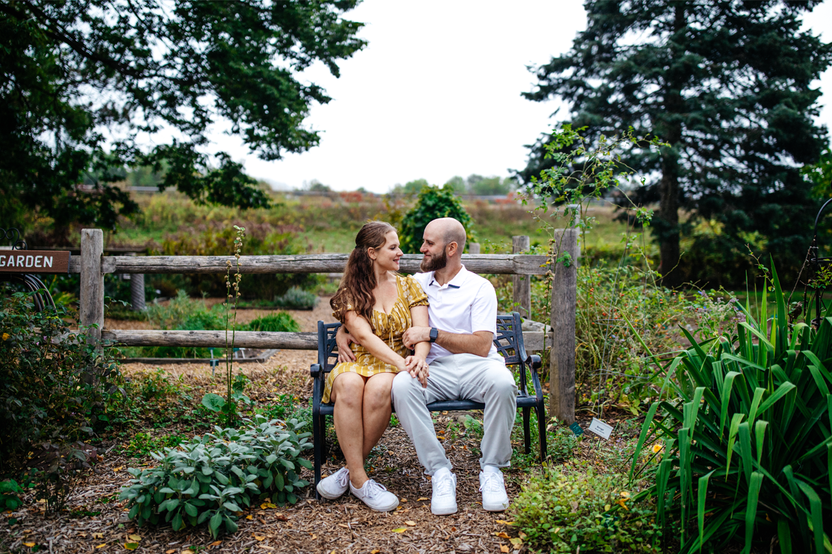 Couple smile at eachother while sitting on bench in Cutler Botanic Garden in Binghamton NY