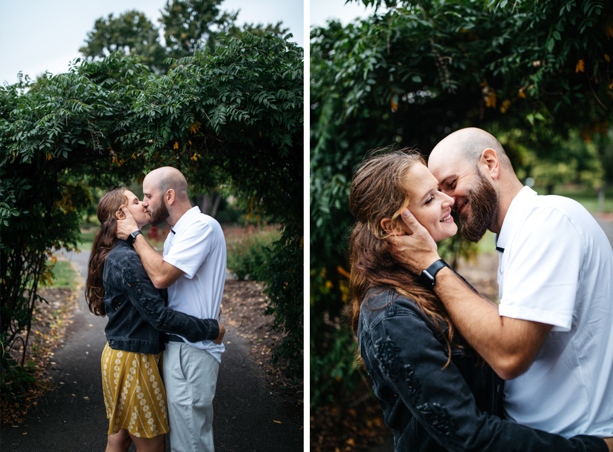 couple kisses in front of leafy arch in botanic garden engagement session