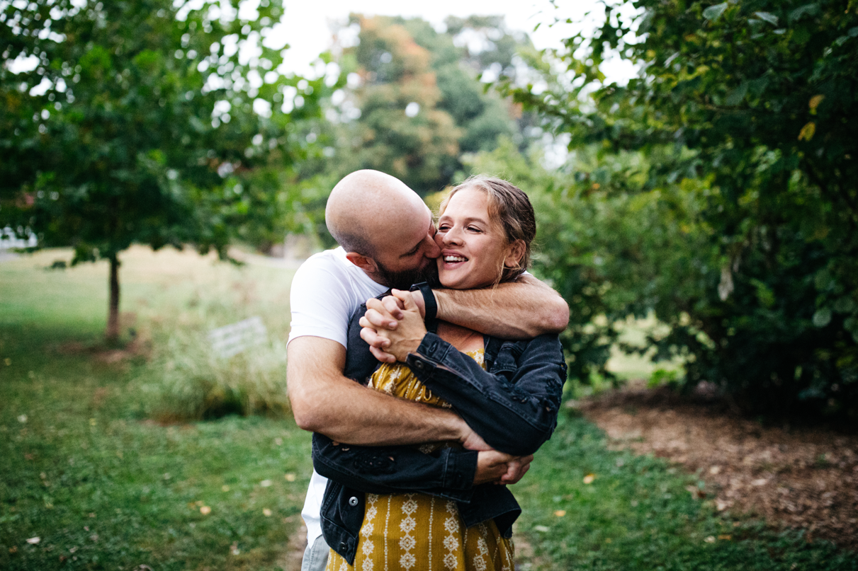man hugs woman from behind while smiling in botanic garden engagement session