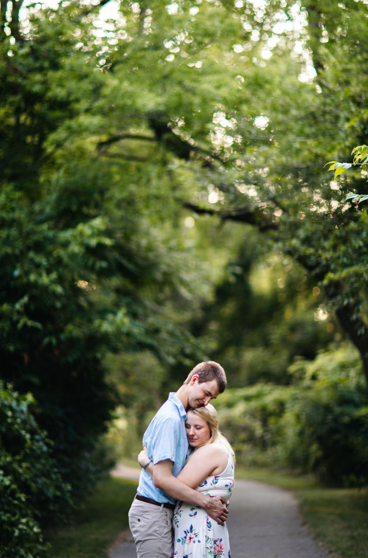 Couple stands on park path and embraces below the trees