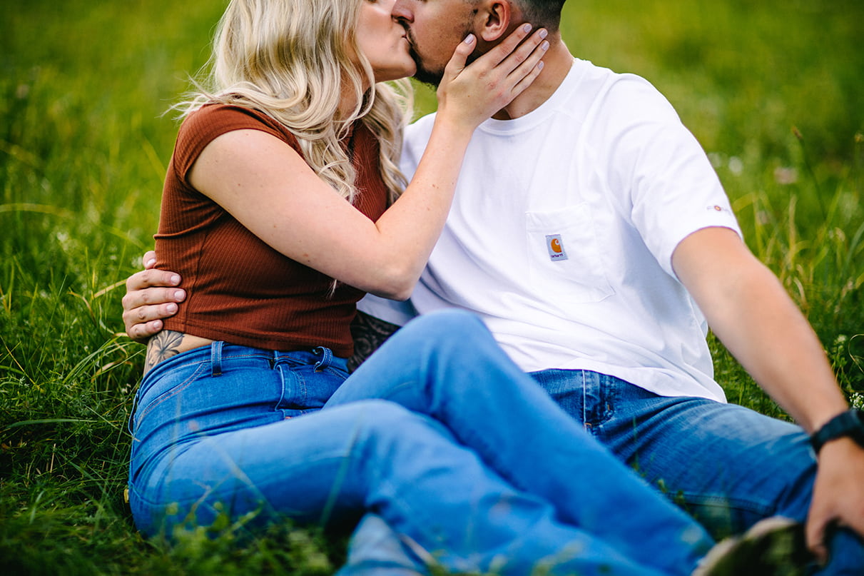 couple kisses while sitting in the grass in a field