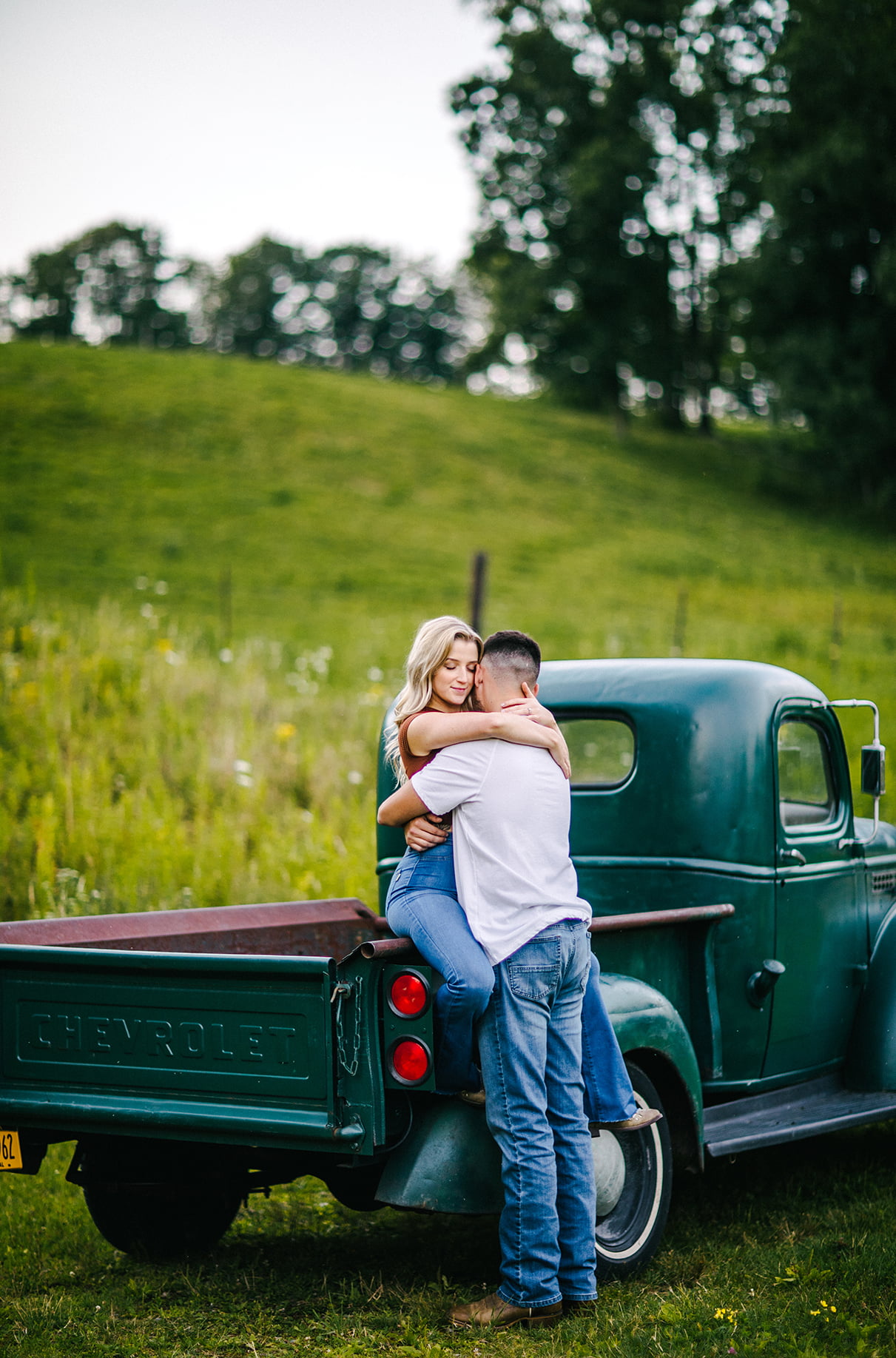 woman sits on the back of a green vintage chevy truck while man embraces her 