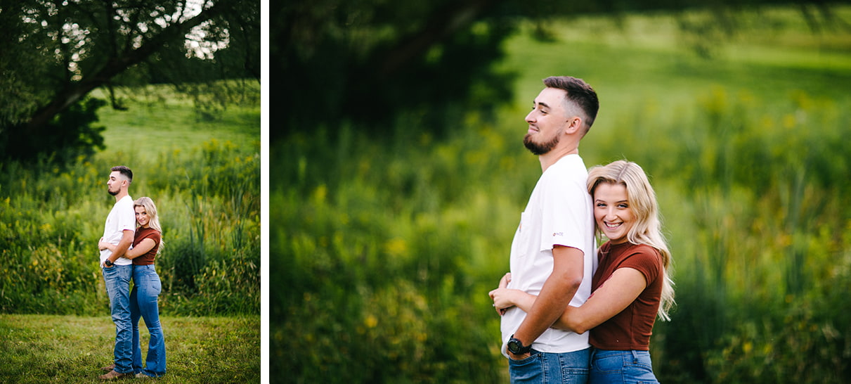 woman hugs man from behind while smiling and standing in front of a grassy hill