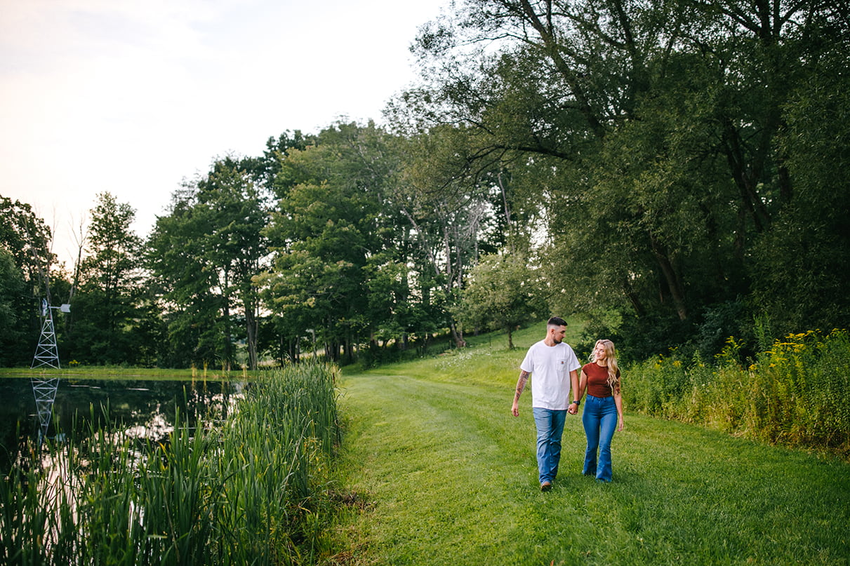 couple walks on path next to pond while holding hands