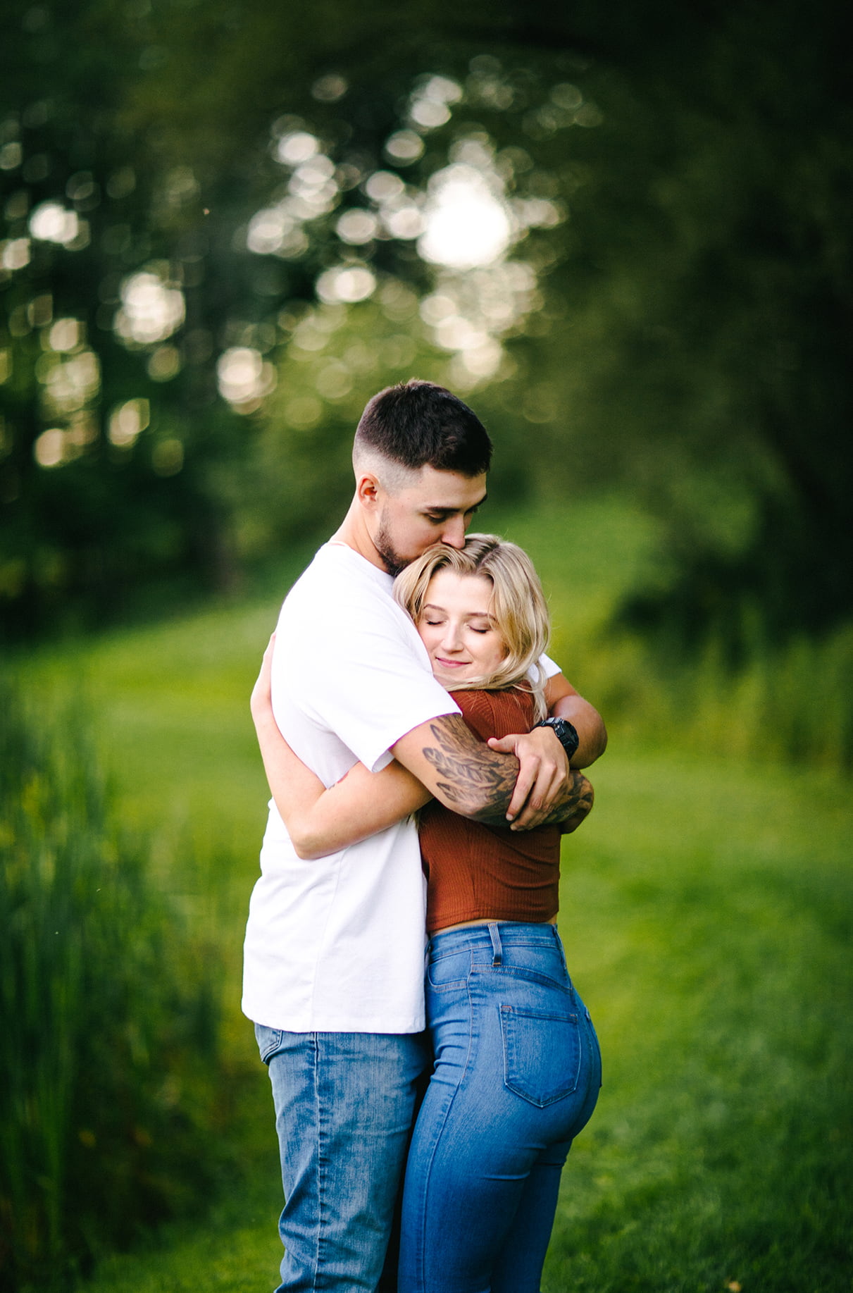 couple hugs each other tight in front of grassy hill while smiling