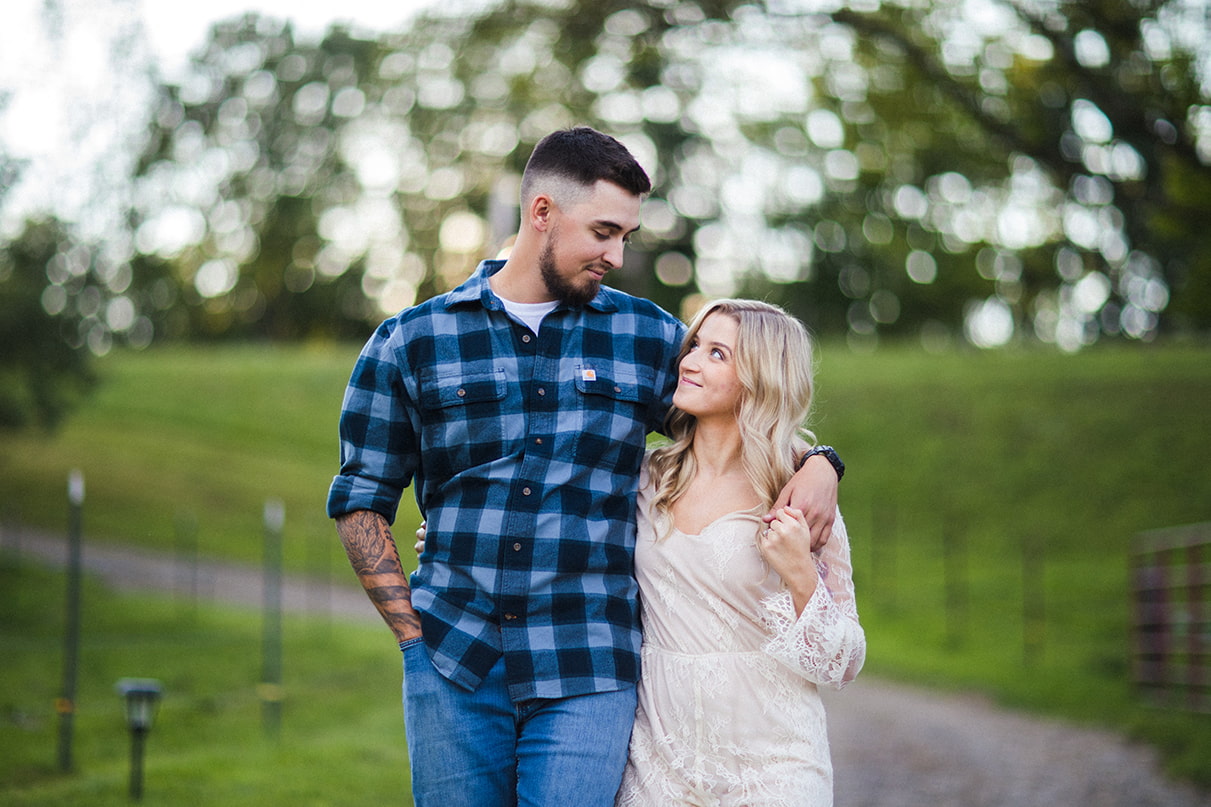 couple looks holds hands while smiling and walking down farm path