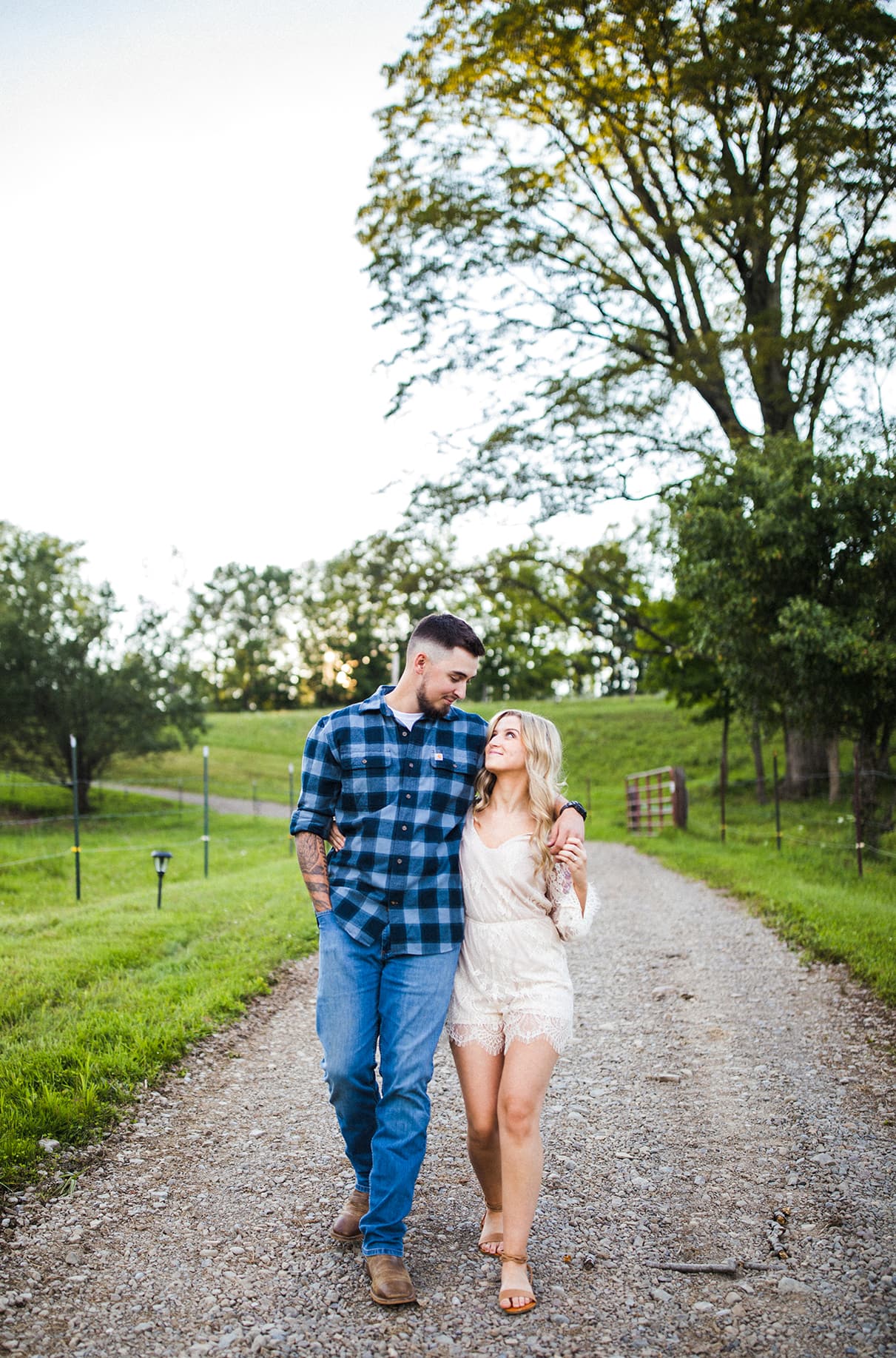 man in blue plaid shirt holds womans hand and walks down farm path