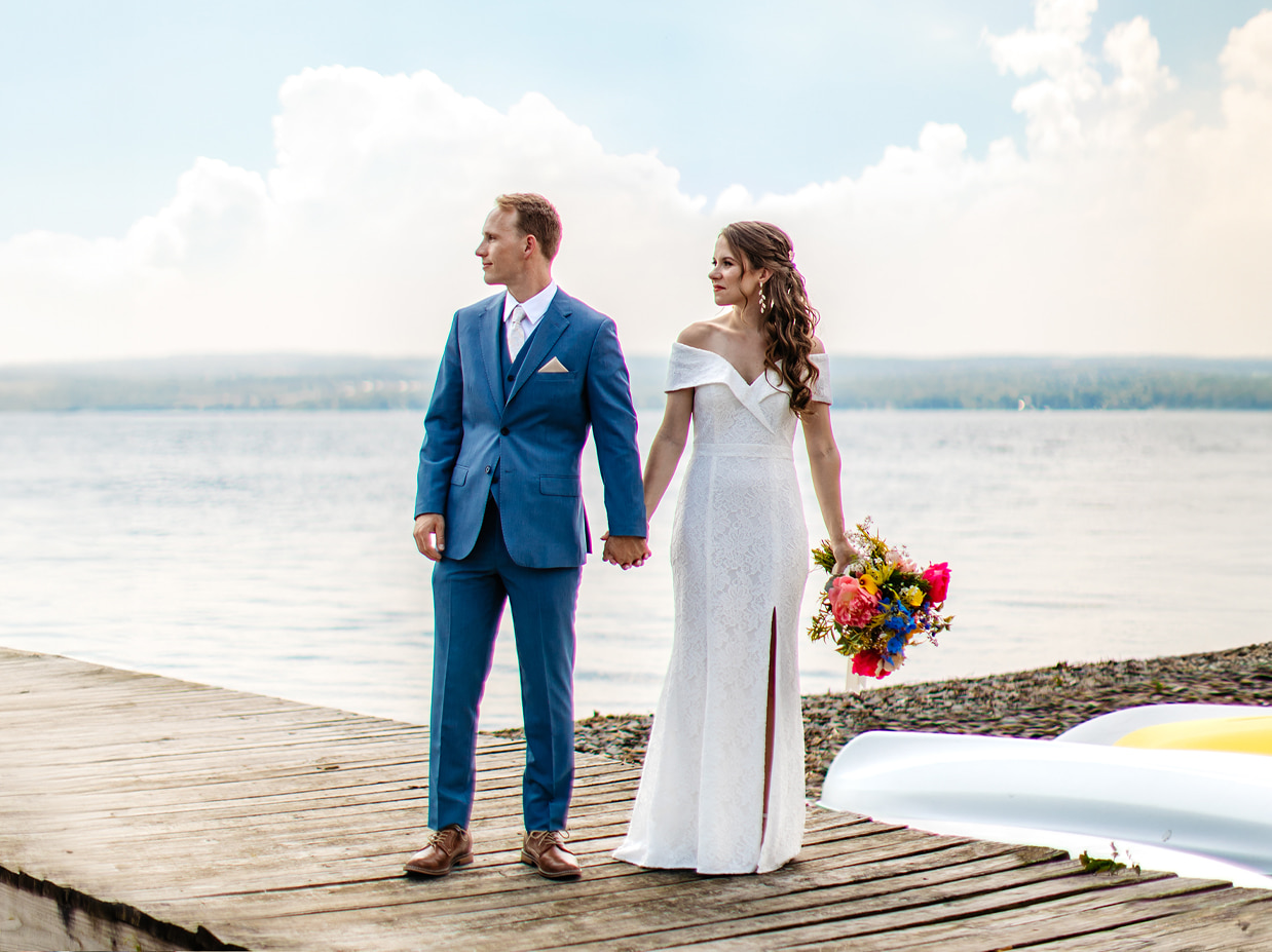 bride and groom stand hand in hand on a dock during their summer wedding in the finger lakes 