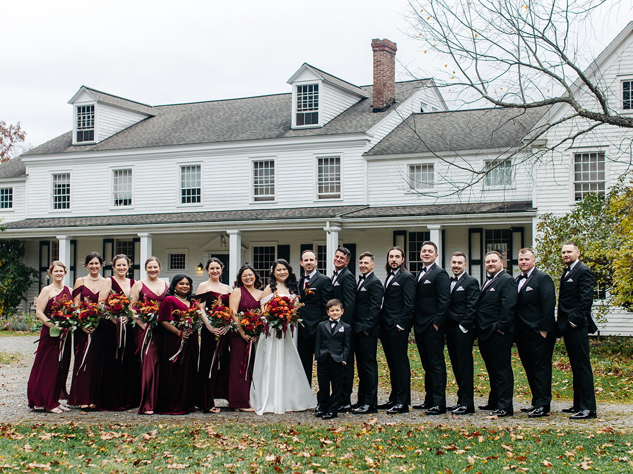 Entire wedding party stands and smiles for photo outside of the Fontainebleau Inn in Alpine NY