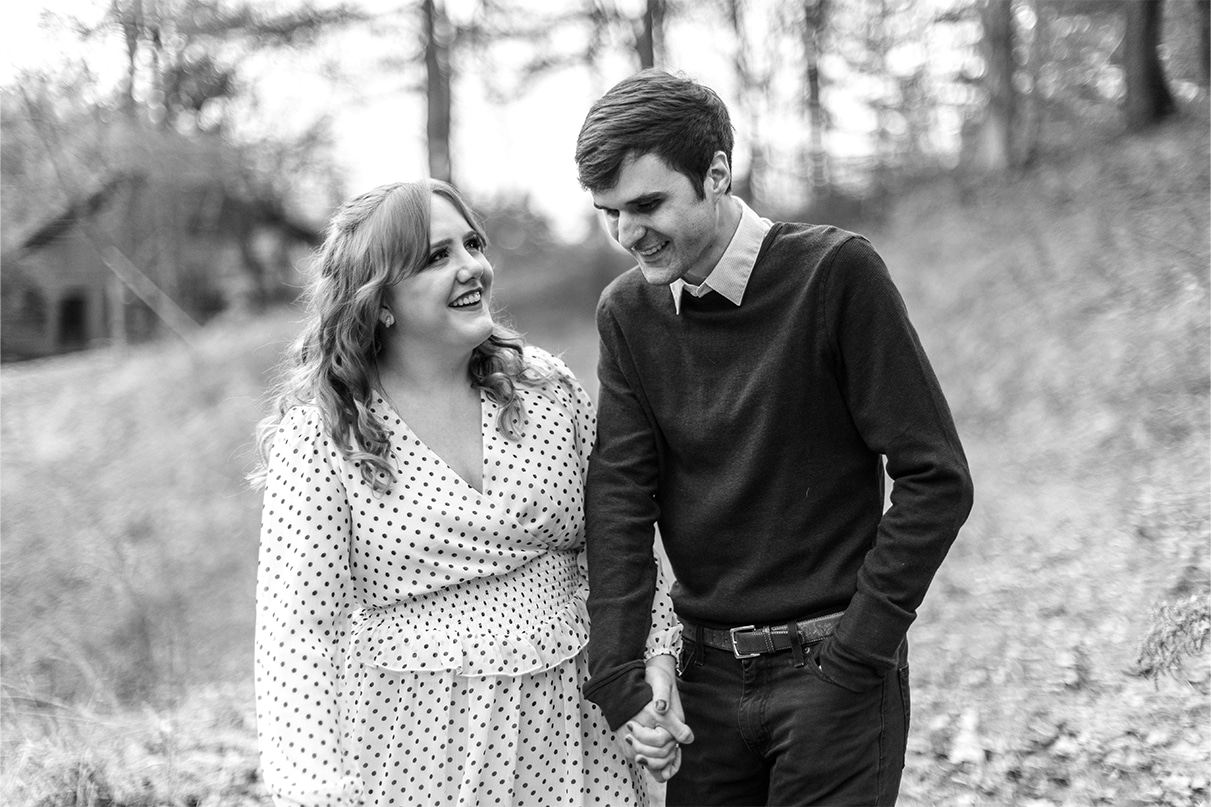 Black and white photo of a couple holding hands and laughing as they walk down a hill in early sprint engagement photos