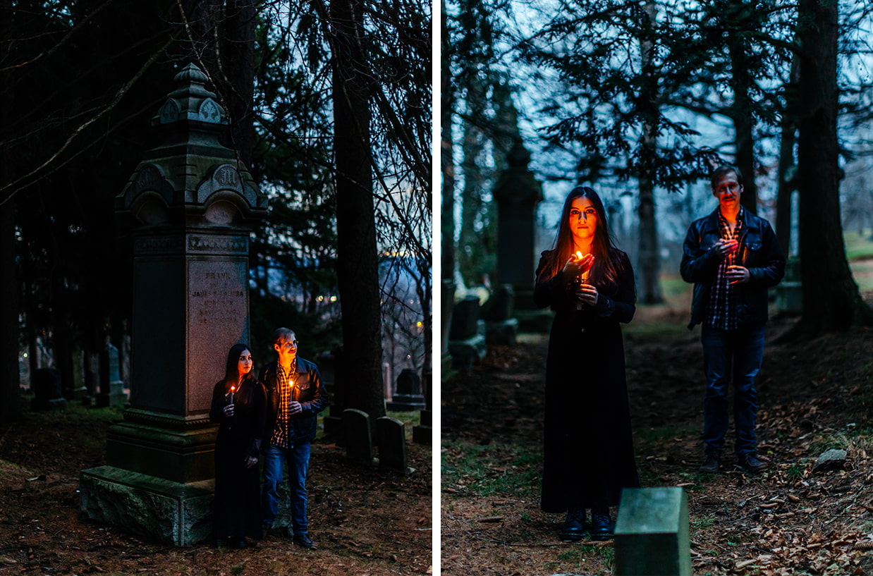 couple poses for halloween engagement or halloween couples photos while holding lit taper candles in a cemetery during twilight