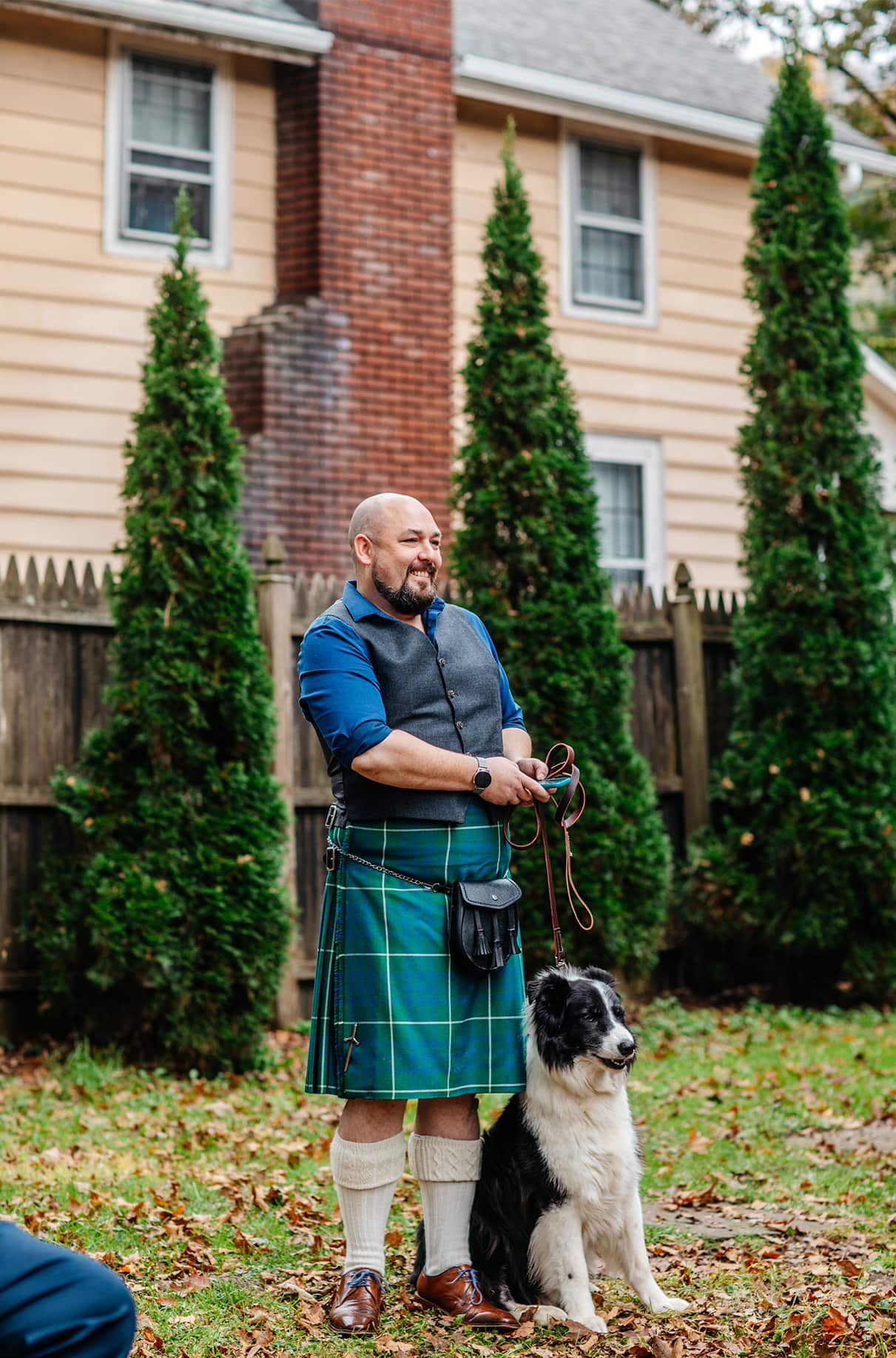 man in kilt smiles while holding the leash of a black and white border collie