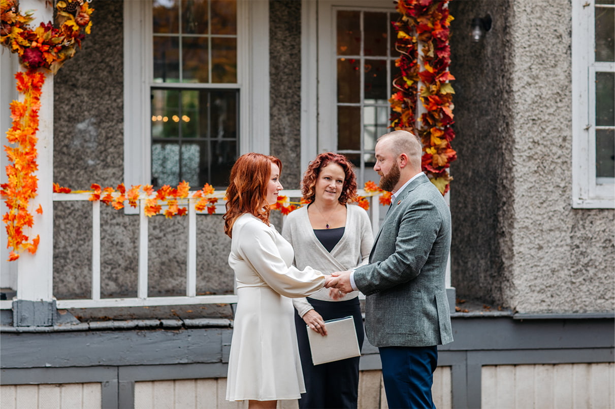 couple stands holding hands in front of officiant