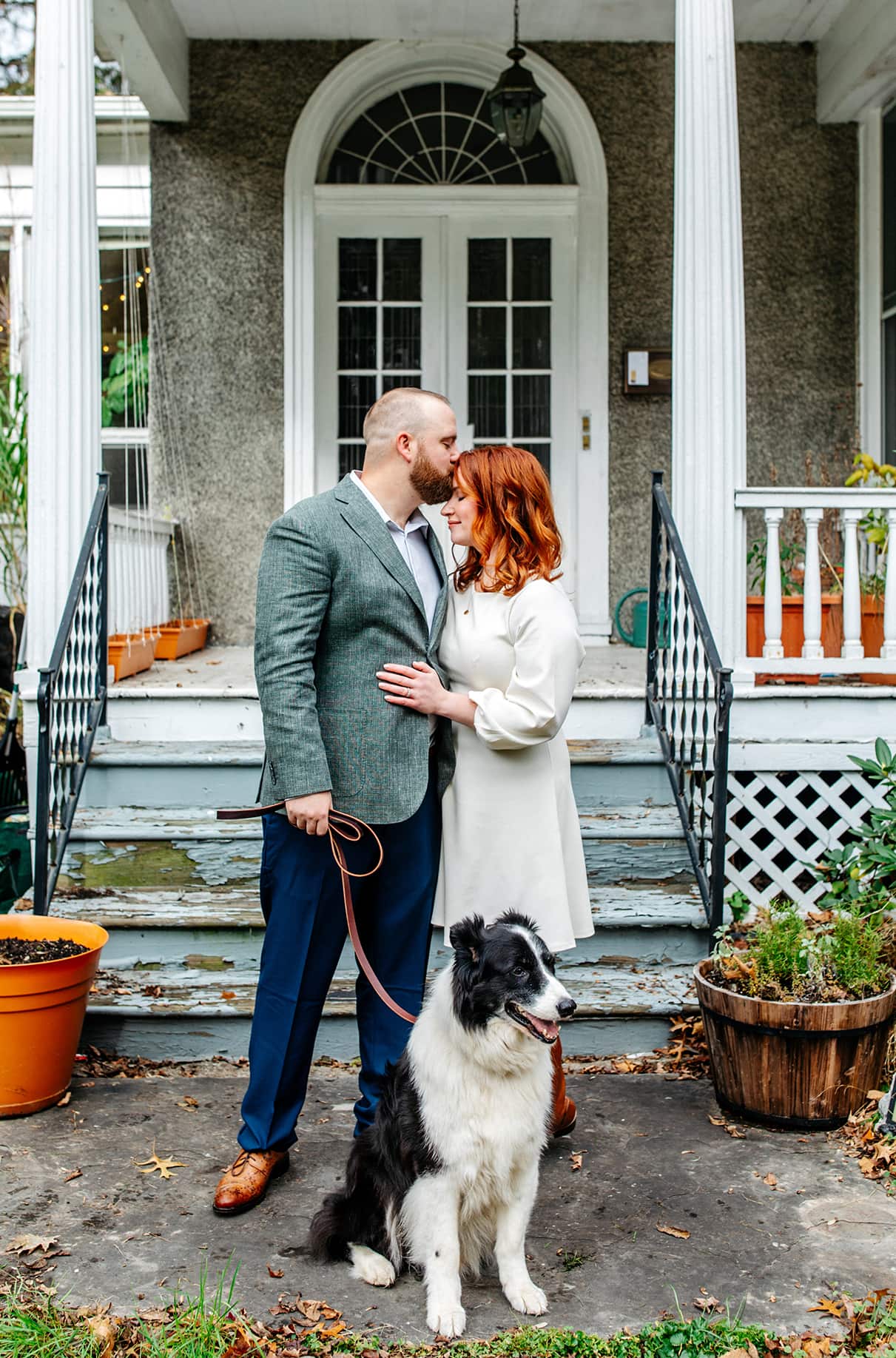 bride and groom stand together in front of pretty house with black and white border collie dog