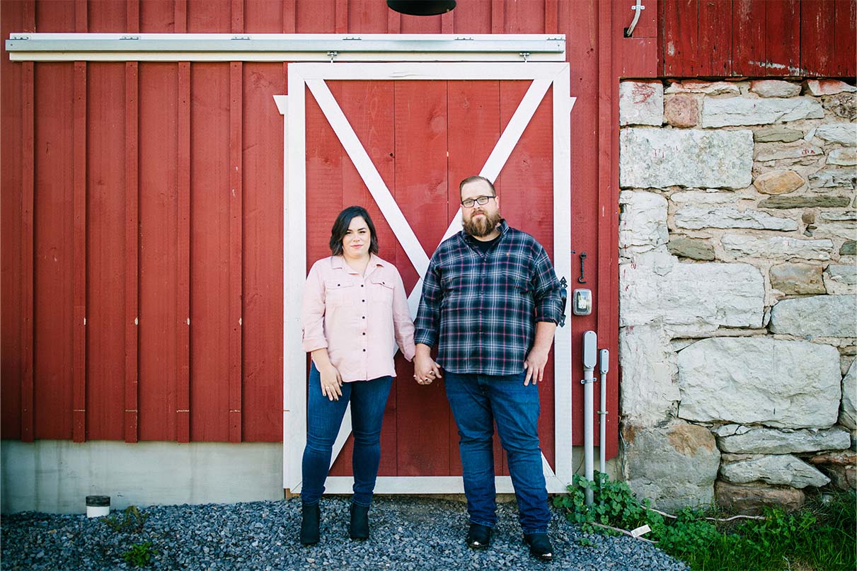 couple holds hands in front of barn door at arlington acres rustic wedding venue lafayette ny