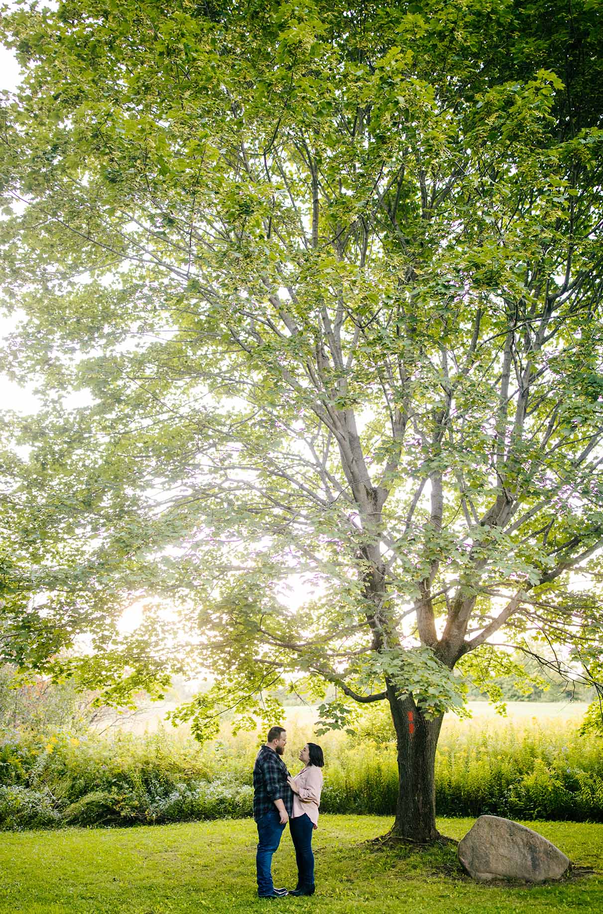 couple stands together under large tree at labrador pond near syracuse ny