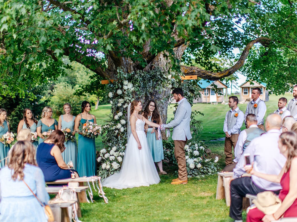 bride and groom have hands tied together during hand-fasting ritual wedding ceremony under a maple tree